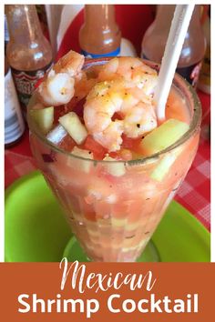 a cocktail with shrimp and cucumber garnish in a glass on a green plate