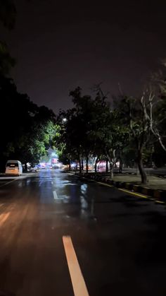 an empty street at night with cars parked on the side and trees lining the road