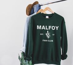 a green sweatshirt hanging on a rack next to a pair of jeans and a hat