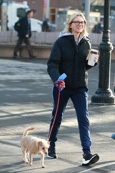 a woman walking her dog on a leash down the street while holding a coffee cup