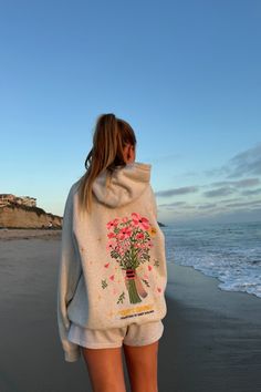 photo shows a blonde teenage girl standing on a sandy beach at sunset. she is facing away from the camera and is looking at the ocean. she is wearing gray sweat shorts and a gray hoodie that has pink embroidered flowers on the back and the words "gift giving" and "courtesy of dandy worldwide." the ocean is to the right of the girl and the sandy beach is to the left. Dandy World Wide Hoodie, Dandy Hoodie Outfit, Dandy Sweatshirt, Merch Ideas Products, Dandy Hoodie, Madhappy Hoodie