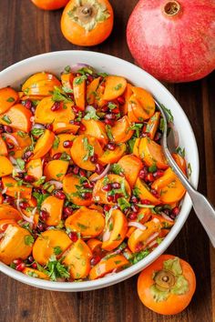 a bowl filled with oranges and pomegranate on top of a wooden table