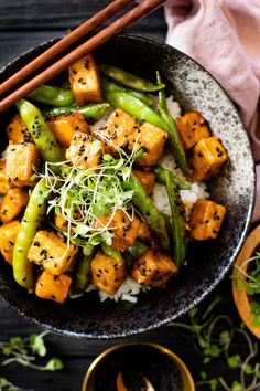 a bowl filled with tofu, green beans and rice next to chopsticks