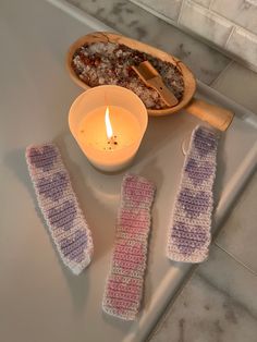 three crocheted mitts next to a lit candle on a counter with other items