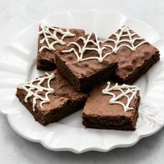 four pieces of brownie on a white plate with spider web decorations and icing