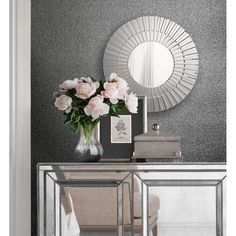 a white dresser topped with flowers next to a mirror and vase filled with pink roses