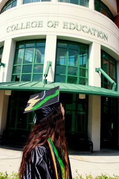 a woman wearing a graduation cap and gown standing in front of a building that says college of education