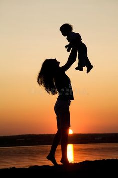 a woman holding a baby up in the air while standing next to a body of water