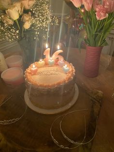 a birthday cake with lit candles sitting on a table next to some flowers and candles