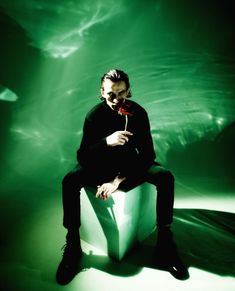 a man sitting on top of a cube holding a flower in his hand and looking at the camera