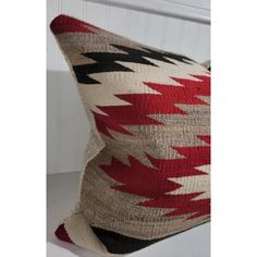 a red, black and white pillow sitting on top of a wooden table next to a wall