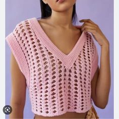 a woman wearing a pink crochet top and holding her hand on her shoulder