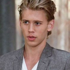 a young man with blonde hair wearing a gray suit and white shirt is looking at the camera