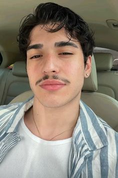 a man with a moustache on his face sitting in a car looking at the camera