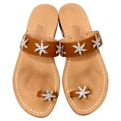 These charming Brown Leather Sandals with Rhinestone Embellished Starfish Accents bring a touch of coastal flair and glamour to any summer wardrobe. Crafted from supple brown leather, these flat sandals feature a stylish ankle strap adorned with three large, sparkling starfish made of dazzling rhinestones that catch the light beautifully. An additional rhinestone-encrusted starfish graces the big toe strap for an extra dash of whimsy. Perfect for beach outings or casual brunches, these sandals can be styled effortlessly with a vibrant maxi dress from Oscar De La Renta or paired with airy linen shorts and a cropped top from The Row for a relaxed yet chic vibe. Complete the look with a woven handbag from Loewe to embody that effortlessly elegant summer aesthetic. Designer Size: Italian 9 / U Beach Embellished Leather Sandals, Luxury Starfish Charm Star Jewelry, Luxury Leather T-strap Sandals For Beach, Leather T-strap Sandals With Buckle For Beach, Multicolor Star-shaped Jewelry With Starfish Charm, Aesthetic Designer, Stella Marina, Brown Leather Sandals, Linen Shorts