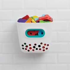 a white basket filled with lots of toys on top of a tiled wall next to a toilet