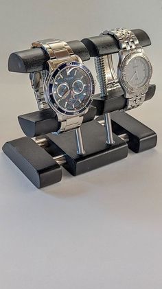 two watches are sitting on black stand with white background and one is displaying the watch