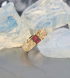 a gold ring with two red stones on top of ice cubes in the background