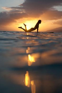 a woman laying on top of a surfboard in the middle of the ocean at sunset