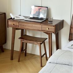 a laptop computer sitting on top of a wooden desk next to a chair and bed