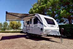 an rv is parked in the dirt near some trees and bushes with a awning over it