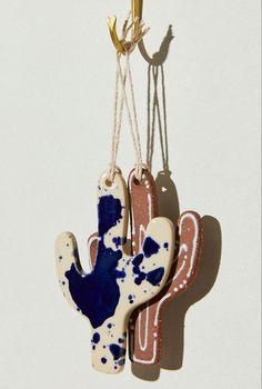 two hand shaped ornaments hanging from strings on a white wall, one with blue and red paint splattered on it