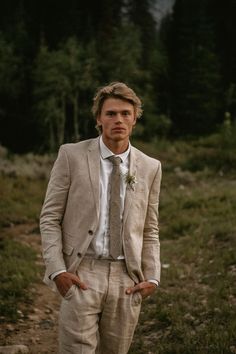 a man wearing a suit and tie standing in the grass with his hands on his hips