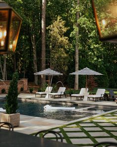 an outdoor swimming pool with lounge chairs and umbrellas in the shade, surrounded by trees