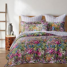 a bed covered in a colorful floral comforter and matching pillowcases with decorative pillows