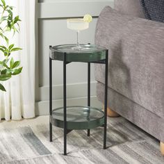 a small side table with a drink on it in front of a couch and potted plant