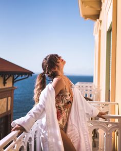 a woman standing on a balcony next to the ocean