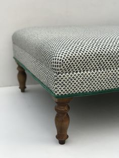 an upholstered footstool with wooden legs and green glass on the top