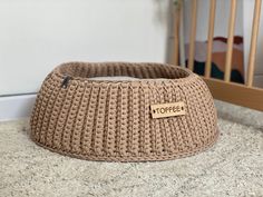 a brown knitted dog bed sitting on top of a floor next to a crib