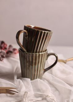 two coffee cups sitting next to each other on top of a white cloth with gold forks