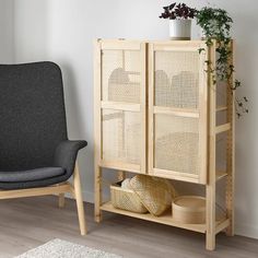 a grey chair and a wooden cabinet with baskets on it next to a potted plant