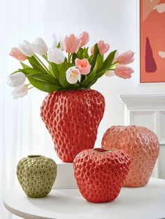 three vases with flowers in them sitting on a table next to two apples and an apple