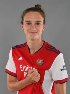 a female soccer player in a red and white uniform poses for the camera with her hands wrapped around her neck