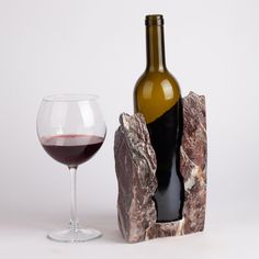 a bottle of wine sitting next to a rock with a glass in it on a white surface