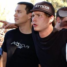 two men in black shirts and hats standing next to each other with one pointing at the camera