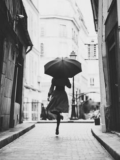 a woman with an umbrella is walking down the street in black and whit photo