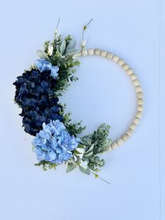 blue flowers and greenery are arranged on a white surface with a beaded necklace