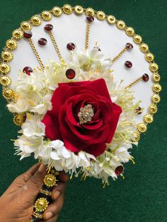 a person holding a red rose and white flowers in their hand on a green surface