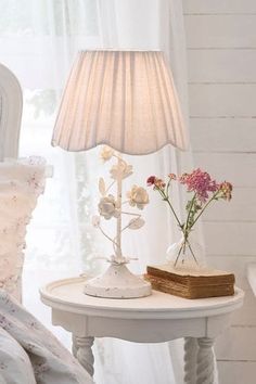 a white table with flowers and a lamp on it next to a bed in a room