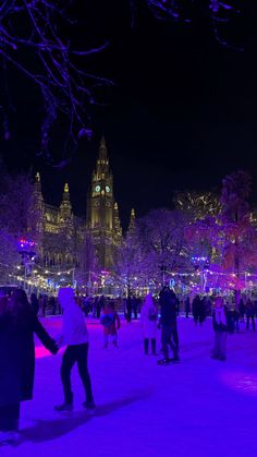 people are skating on the ice at night in front of a large building with lights