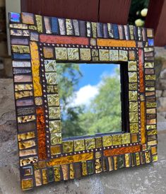 a small mirror sitting on top of a stone counter next to a tree and sky