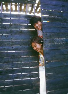 two girls peeking out from behind a wooden fence