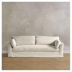 a white couch sitting on top of a hard wood floor next to a gray wall