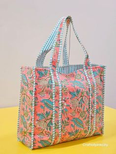 a pink and blue floral bag sitting on top of a yellow table next to a white wall