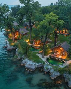 an aerial view of a house on the water with trees around it and lights at night