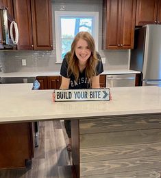 a woman sitting at a kitchen island with a sign on it that says build your bite